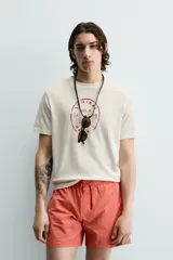 Camiseta de corte regular, color crudo, con cuello redondo y manga corta. Presenta un estampado frontal con diseño circular en tono rojizo con efecto lavado.