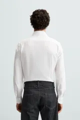Camisa blanca de manga larga con cuello italiano abierto y cierre frontal de botonadura.
