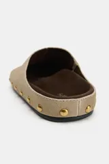 Zapato destalonado tipo mule de serraje en color beige, con punta redonda, suela plana y detalle de tachas metálicas doradas alrededor de la plataforma.