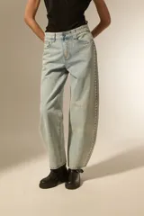 Pantalon de jean estilo baggy, color celeste lavado, con detalle de tachas metálicas en los bolsillos delanteros y a lo largo de las costuras laterales. Presenta un corte ancho y tiro bajo.