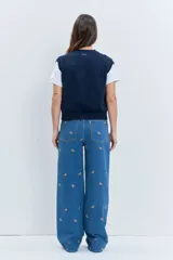 Chaleco de punto rojo con cierre frontal de botones, cuello redondo y dos bolsillos frontales con solapa. Presenta un diseño de tejido acanalado en los bordes y un pequeño parche decorativo en el pecho.