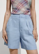 Short celeste de lino con tiro medio, pinzas delanteras, bolsillos laterales y cierre oculto con botón, gancho y cremallera.