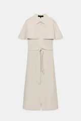 Vestido camisero midi de algodón con diseño de capa, cuello solapa, manga corta tipo capa y trabillas en los hombros. Presenta cierre frontal con botones, bolsillos delanteros y cinturón ajustable del mismo tejido con lazada. El bajo tiene un acabado en línea evasé.