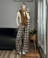 Pantalón tipo palazo de corte amplio y tiro alto, confeccionado en tela con estampado de cuadros escoceses en tonos marrones, blancos y negros. Cuenta con cintura elástica y bolsillos laterales.