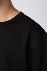 Remera de corte oversize color beige, con cuello redondo y etiqueta decorativa pequeña en el ruedo inferior.