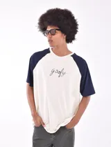 Remera de mangas cortas ranglan, color crudo con mangas azul marino y estampado frontal con la palabra "goofy" en cursiva.