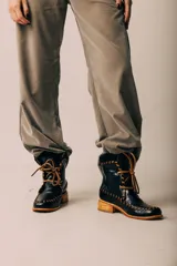 Botas de cuero negro de caña corta con cordones y costuras artesanales en hilo marrón claro, suela de madera con taco bajo y detalle de corderito en el borde superior.