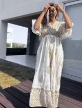 Túnica larga de estilo boho, color crudo con estampado de arabescos y detalles en hilo dorado. Presenta escote en V, mangas amplias tipo kimono y cordón ajustable en la cintura con borlas decorativas.