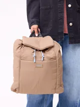 Mochila de diseño acolchado en color beige, con solapa superior, cierre de cordón ajustable y bolsillo frontal con parche de la marca Rusty Supply.