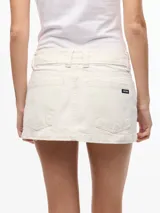 Minifalda de gabardina blanca de tiro bajo, con diseño de cinco bolsillos, trabillas anchas para cinturón y dobladillo deshilachado.