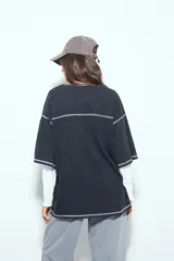 Remera de manga corta color marrón con efecto desgastado, corte oversize y costuras a la vista en color blanco. Presenta cuello redondo con cuello polo blanco superpuesto y mangas largas a rayas horizontales marrones y blancas por debajo.