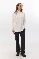 Polera de tejido acanalado en color blanco, con cuello alto, mangas largas y diseño de corte recto con aberturas laterales en el ruedo.