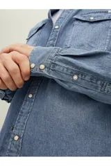 Camisa de denim celeste de manga larga, con cuello clásico, cierre frontal con botones a presión y dos bolsillos con solapa abotonada en el pecho.