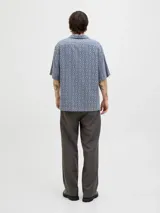 Camisa de manga corta con estampado geométrico en tonos azul y beige, cuello resort y cierre de botones. Confeccionada en tejido dobby 100% algodón.