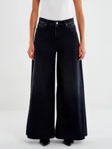 Jeans de denim negro con lavado oscuro, tiro alto y pierna muy ancha (palazzo o culotte muy largo). Presenta cierre clásico de botón y cremallera, y bolsillos delanteros y traseros.