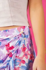 Short con diseño de pollera, tiro medio, estampado floral en tonos violeta, azul y rosado. Presenta detalle de aro de madera en la cintura, cierre lateral oculto y volados en la parte inferior.