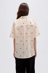 Camisa de lyocell color beige con estampado de lunares negros, cuello solapa, manga corta y cierre frontal con botones.