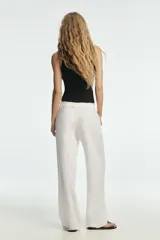 Pantalón blanco de tiro medio con pierna ancha y tejido que contiene lino. Presenta cintura con trabillas y un cinturón ajustable con lazada del mismo tejido. Cierre frontal con cremallera y botón.