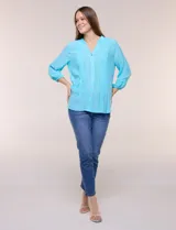 Blusa celeste de silueta suelta y textura liviana, con escote en V, cuello mao y cierre frontal de botones. Cuenta con alforzas verticales en el pecho y mangas tres cuartos con puños elastizados y detalle de galón calado.