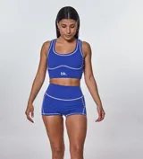 Conjunto deportivo compuesto por un top de escote redondo y un short de tiro alto, ambos en color azul con costuras decorativas a la vista en color blanco. El top presenta el logo de la marca estampado en el frente.