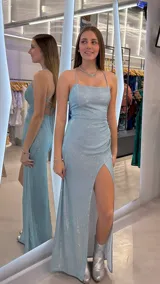 Vestido largo celeste con acabado brillante, tirantes finos cruzados en la espalda, tajo lateral en la pierna y fruncido en la cadera.