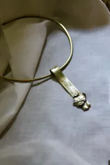 Gargantilla rígida dorada con dije rectangular irregular de bronce.