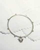 Brazalete esclava rígido de plata con pequeñas esferas distribuidas a lo largo del aro y un dije colgante en forma de corazón.