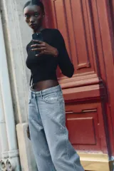 Top corto y ajustado de punto canalé color negro, con cuello redondo, manga larga y detalle de aplique metálico en la parte delantera.