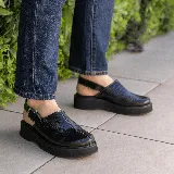 Sueco de cuero vacuno color marrón con estampado de cocodrilo, suela de goma negra y hebilla metálica plateada.