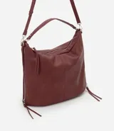 Bolso tipo hobo de gran tamaño en color bordó, confeccionado en poliuretano. Presenta una estructura desestructurada, cierre superior, correas dobles (una de mano y una larga desmontable) y cierres laterales decorativos con tiradores.