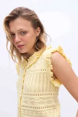 Chaleco tejido de punto color amarillo, con diseño calado, escote redondo y volados en los hombros y cuello. Cuenta con cierre frontal de botones forrados al tono.