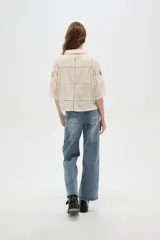 Camisa de algodón color crudo con diseño de paneles unidos por cintas caladas. Presenta bordados florales en cada panel, cuello camisero, cierre frontal con botones y mangas tres cuartos.