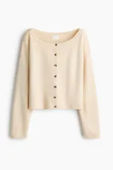 Saco corto de punto suave en color beige, con diseño de hombros caídos y escote amplio ribeteado. Cuenta con mangas largas y cierre frontal de botones con efecto carey.