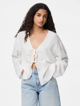 Blusa blanca de algodón con escote en V y mangas largas abullonadas. Presenta cierre frontal con lazos.