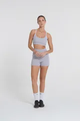 Top deportivo gris con tirantes blancos regulables, escote medio y compresión media. Confeccionado con tejido Activelu con nula transparencia.
