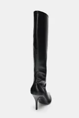 Bota de caña alta ajustada con acabado en punta y tacón fino. Presenta detalle de pespunte en el cuerpo y cierre mediante cremallera lateral.