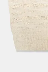 Jersey de punto color crema, sin mangas (manga sisa) con hombreras marcadas y cuello redondo. Presenta textura de tejido con líneas horizontales en relieve.