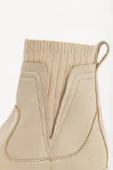 Bota tipo chelsea de caña media en color beige, con suela track dentada y paneles laterales elásticos acanalados.