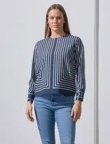 Blusa de gasa estampada con líneas verticales negras sobre fondo beige, de manga larga con puño abotonado. Espalda con abertura y botón.
