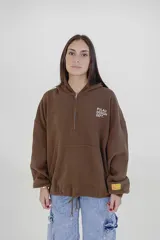 Canguro color marrón con cierre frontal parcial, capucha y bolsillo tipo canguro. Presenta el logo de la marca estampado en el pecho y una etiqueta decorativa en el puño.