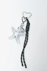 Llavero con mosquetón en forma de corazón, cordón negro trenzado con detalles blancos y dijes colgantes plateados de estrella de mar y concha marina.