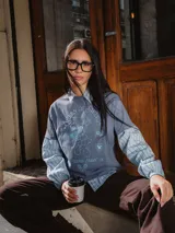 Remera de manga larga con diseño superpuesto que simula una camisa de rayas debajo. La prenda principal es de color azul piedra con estampado gráfico de Minnie Mouse y texto alusivo al tenis, mientras que las mangas y el cuello son de tela camisera a rayas celestes y blancas.