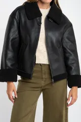 Campera tipo gamulán de cuero sintético negro con interior y detalles de cuello y puños en corderito negro. Presenta cierre frontal y diseño oversize.