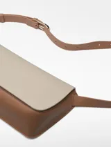 Riñonera de piel bovina en dos tonos: base marrón y solapa color crema. Tiene un compartimento principal con cierre magnético oculto bajo la solapa y un bolsillo interior. Incluye un asa larga regulable para llevar cruzada o como riñonera.