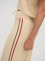 Pantalón de punto color verde oliva, confeccionado en algodón, con corte holgado, pierna ancha y tiro alto. Cuenta con pretina elástica con cordón de ajuste y una línea lateral a contratono en color naranja.