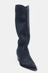 Bota alta de estilo cowboy confeccionada en serraje de color azul marino, con tacón medio en bloque y puntera perfilada. Presenta costuras decorativas en el cuerpo y diseño de calce fácil.