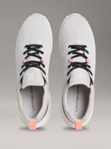 Zapatillas Calvin Klein modelo Eva Runner de color gris, confeccionadas en malla técnica transpirable con detalles en negro y salmón. Presentan suela blanca de EVA ultraligera, cordones negros y el logo 'cK' en el talón.