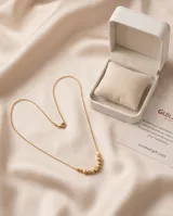Collar de cadena fina con baño de oro, adornado con una serie de pequeñas esferas y un cubo central.