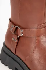 Bota biker negra de símil cuero, con punta redonda y apliques de tachas, hebilla y argolla. Plataforma tractor de 5cm y cierre lateral.