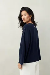 Sweater de tejido de punto color blanco hueso, con cuello redondo y mangas acampanadas. Presenta una hilera de botones a tono en el lateral de cada manga.